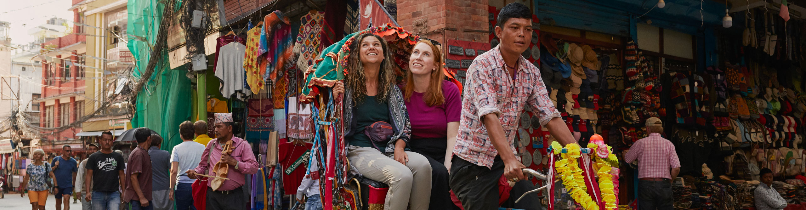 Women on tuk tuk riding through colourful busy market street in Kathmandu, Nepal 