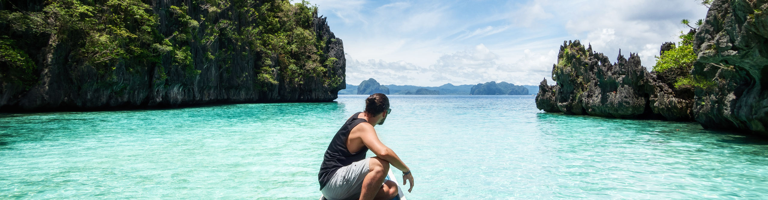 El Nido, Palawan, Philippines, traveler sitting on boat with sparkling turquoise water on sunny day.