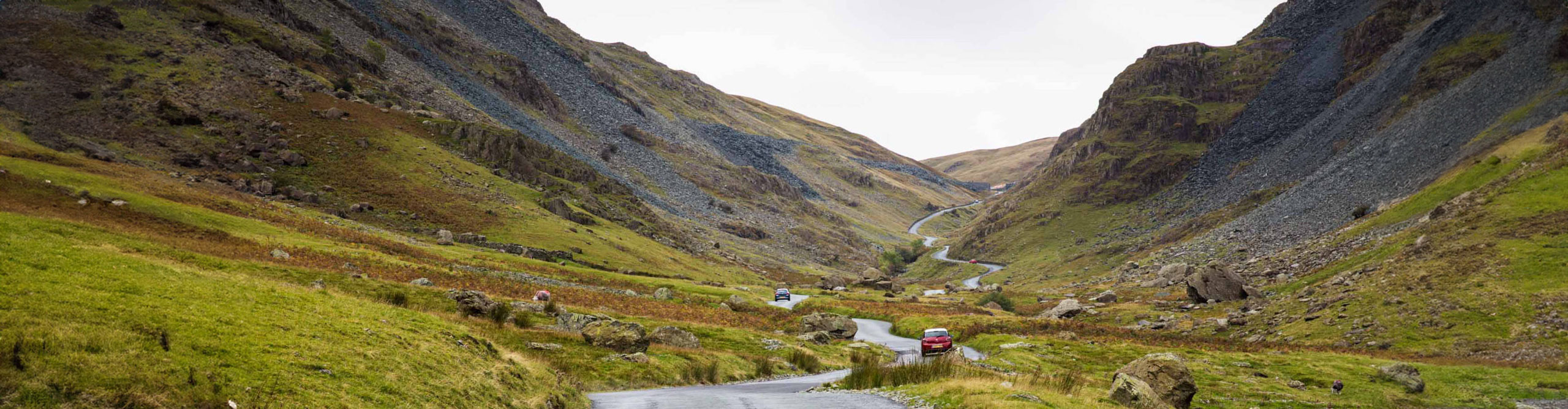 Car driving on road through between foothills of the Lake District, England 