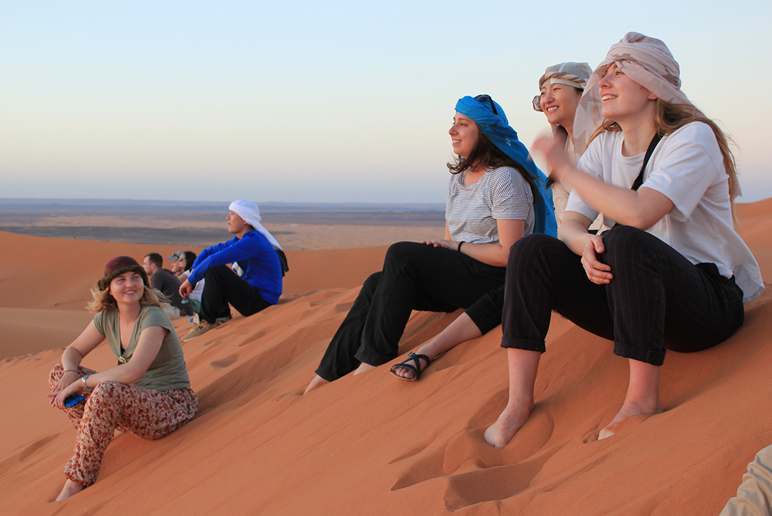 Group of travellers watching the sunset in the Sahara desert in Morocco