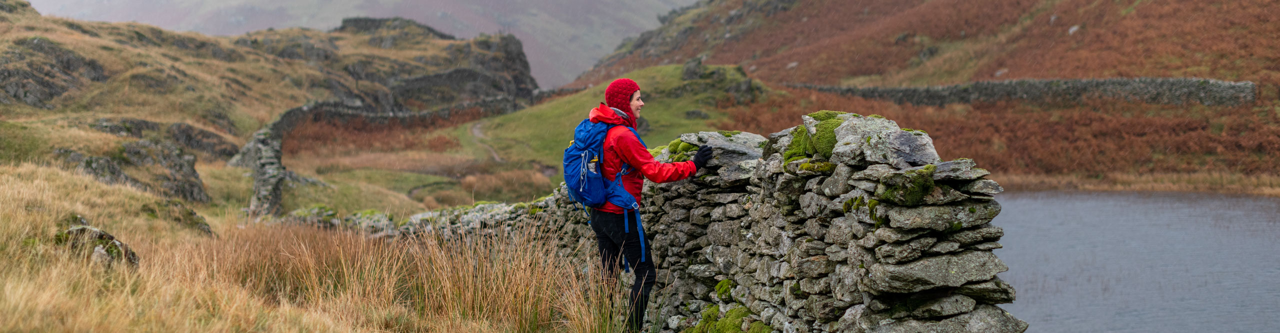 Woman  in red jacket overlooking the lake whilst hiking in the Lake District, UK