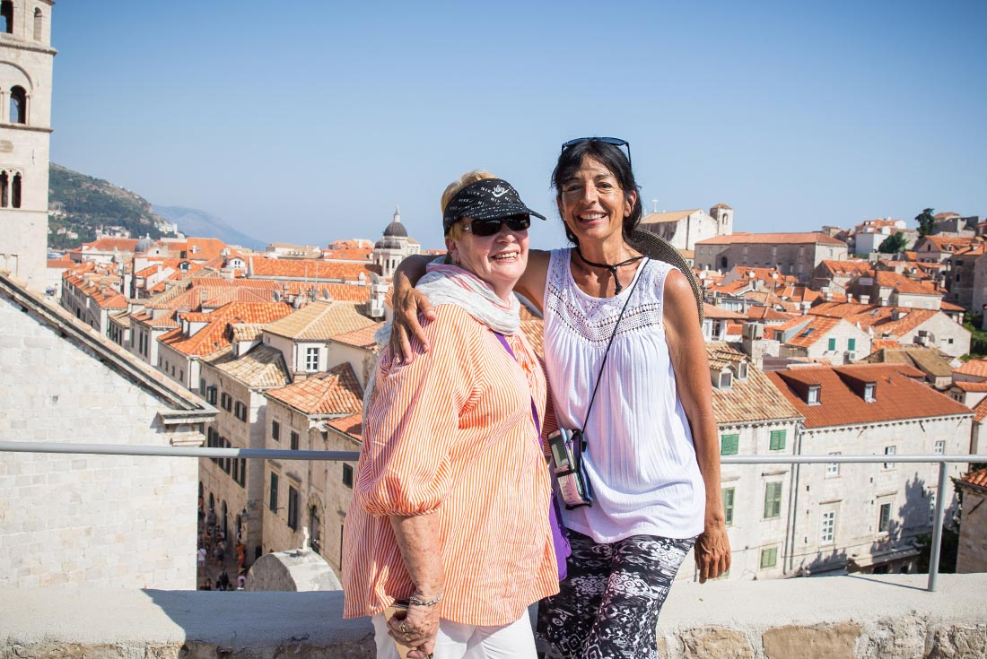 Two travellers posing and smiling in front of old Dubrovnik architecture, Croatia