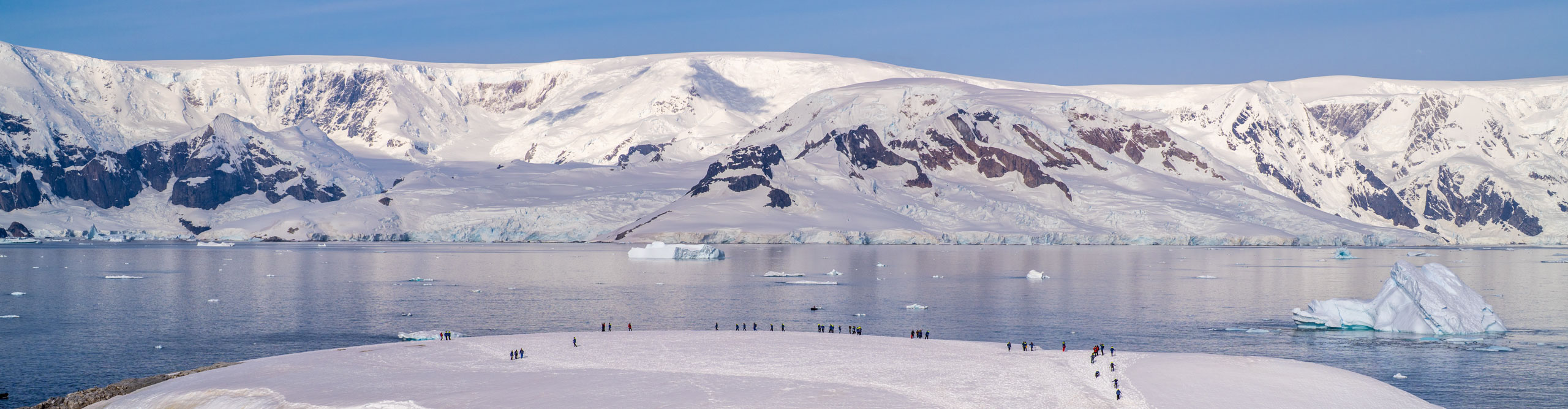 View of the water, hills, snow and ice with people on the shoreline in Antarctica 