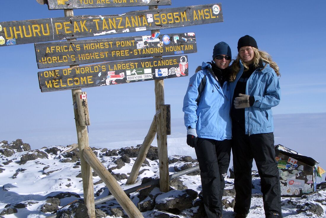 Hikers stand by sign as they reach peak of Mount Kilimanjaro with snow covered ground behind them