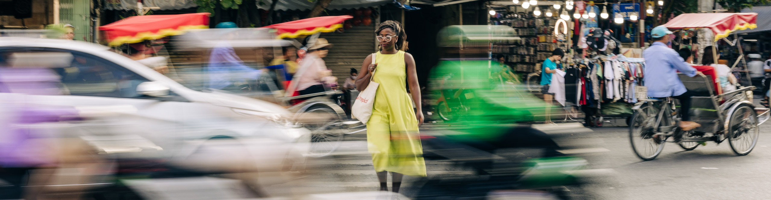 Woman in yellow dress standing in busy street with mopeds driving past, Hanoi, Vietnam