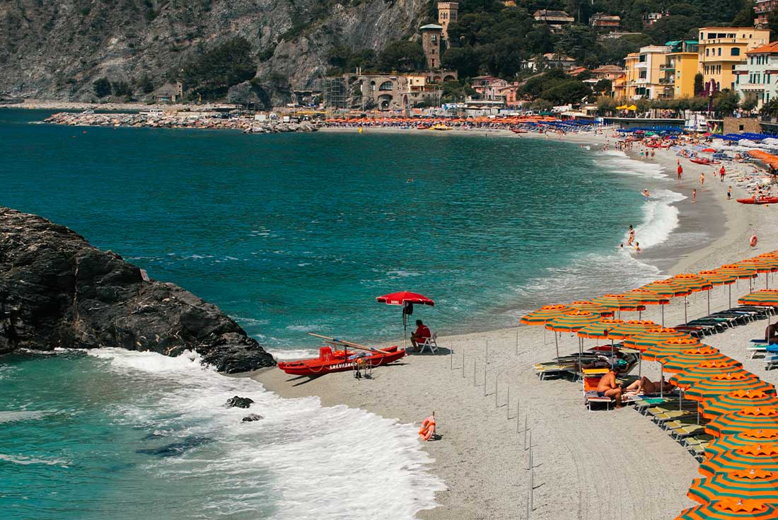 Coastline of Cinque Terre lined with orange and green striped umbrellas 