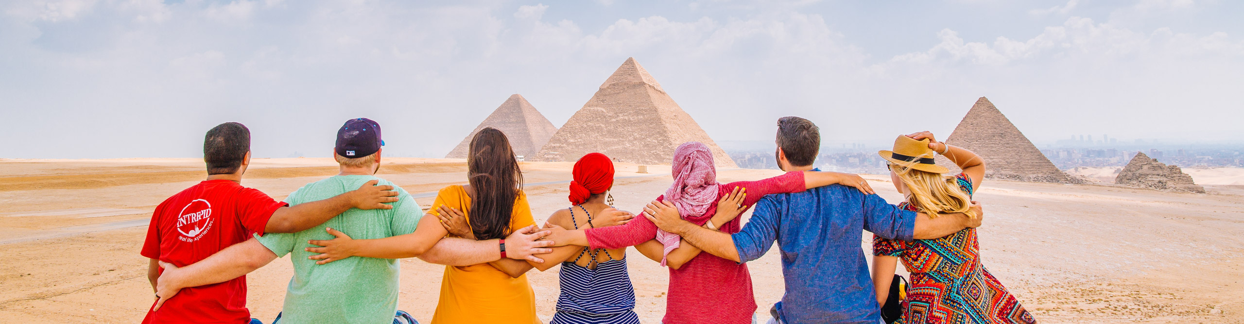 Group in colourful clothing hugging whilst looking at the Pyramids in Egypt on a clear day 
