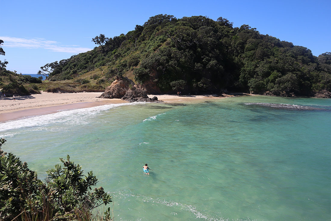 View of Matapouri beach with swimmer in the water and green hills surrounding