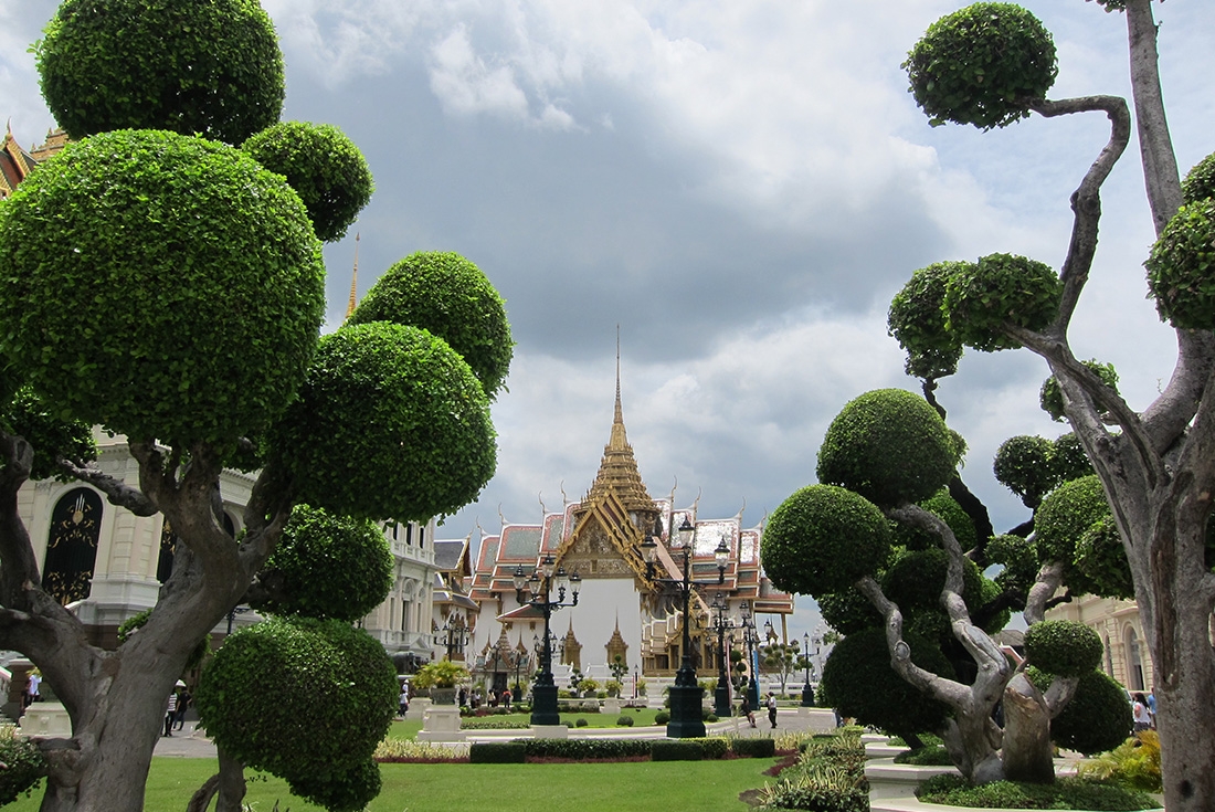 The Grand Palace framed by manicured tress on the grounds in Bangkok, Thailand.