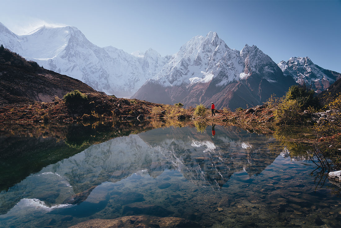 A hiker looks out at the Himalayas from a pond near Bimthang village on the Manaslu Circuit