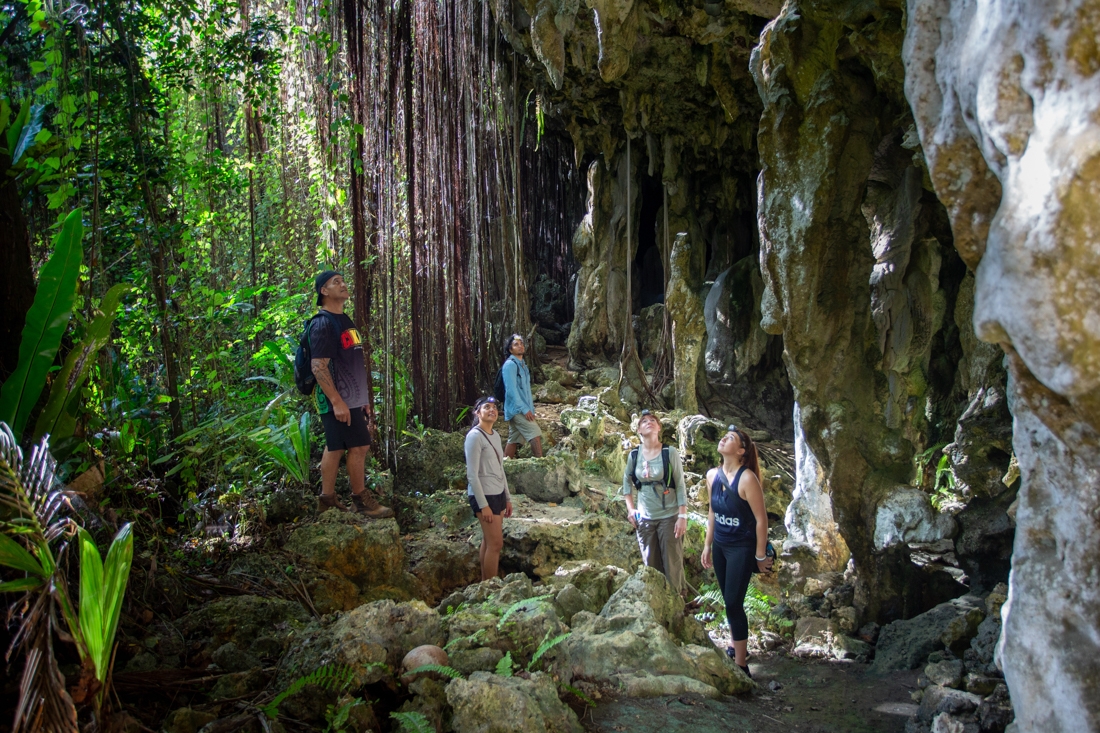 Intrepid travellers stand amazed at the entrance of Anatakitaki cave, Atiu Island, Cook Islands