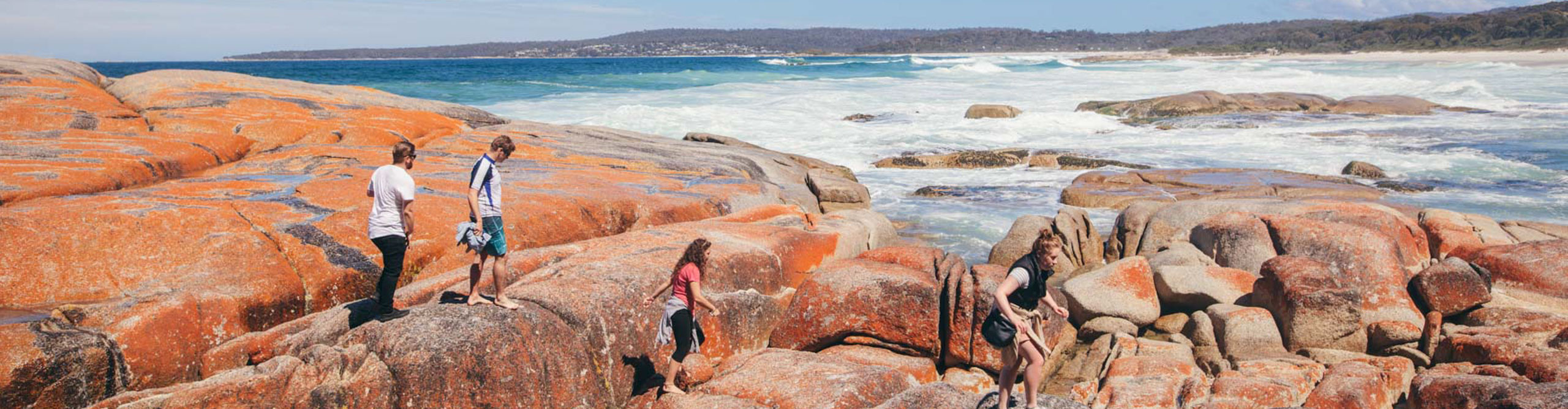 People walking on the red rocks of the bay of fires in Tasmania, Australia 