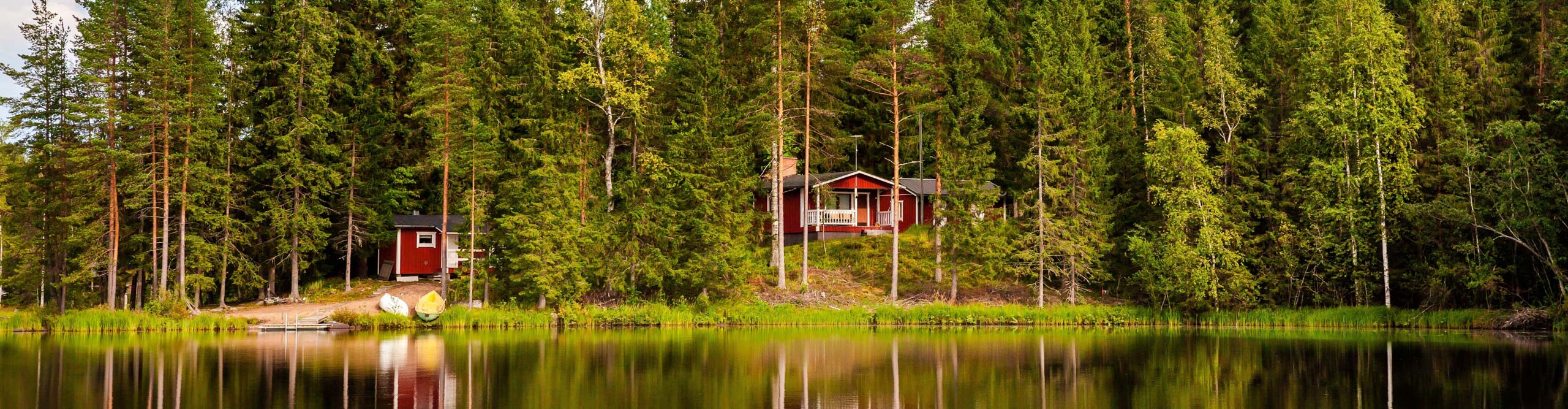 Red wooden cottage amongst the trees reflected in the lake in rural Finland