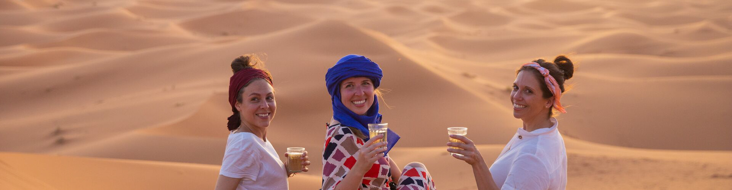 Women drinking wine in the Sahara Desert in the late afternoon sun, Morocco 