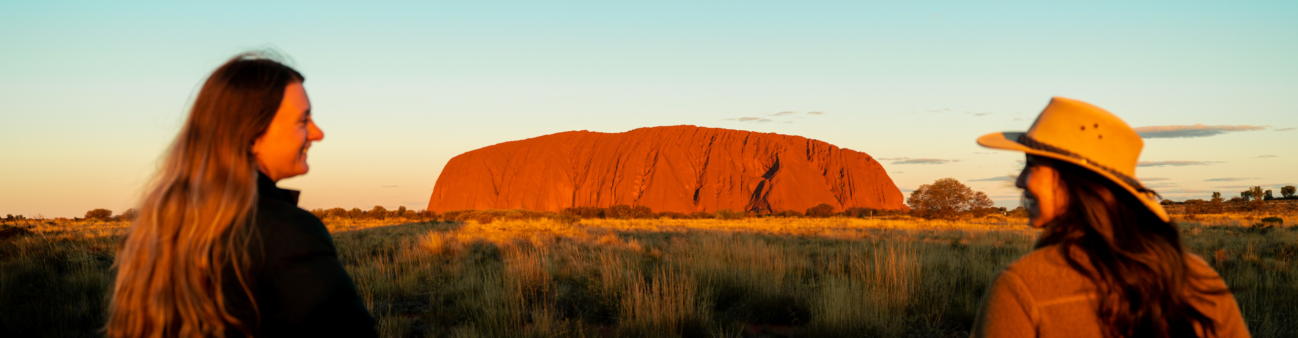 Uluru at sunset with two women looking happily across at each other