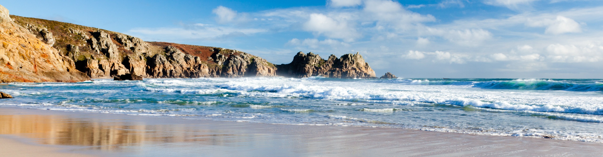 Waves crashing on a sandy beach in the late afternoon on a sunny day,  Porthcurno, Cornwall, UK