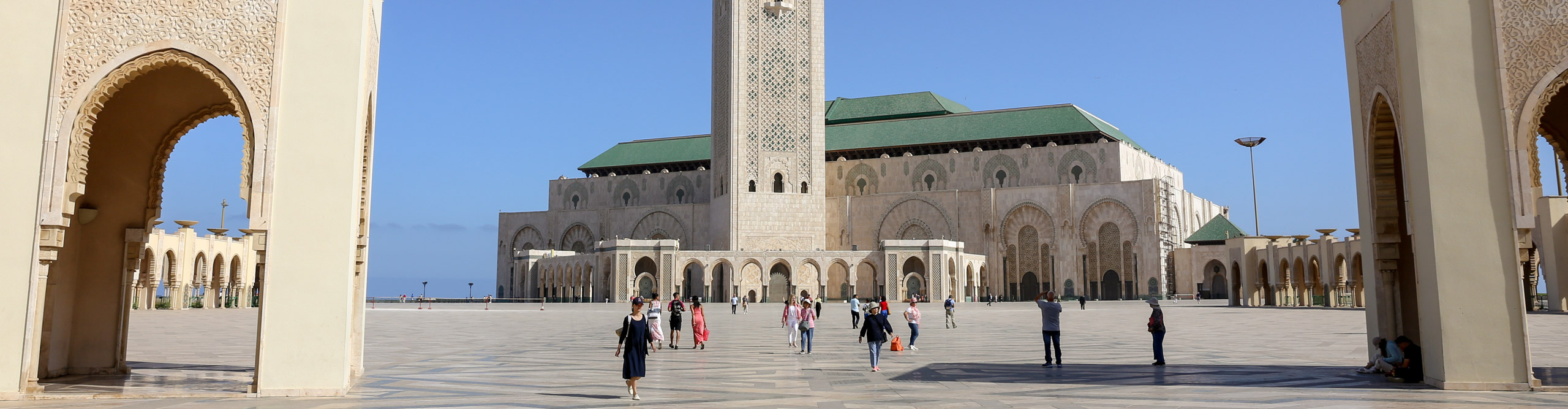 People walking outside the Hassan Mosque, with a clear blue sky, in Casablanca, Morocco 