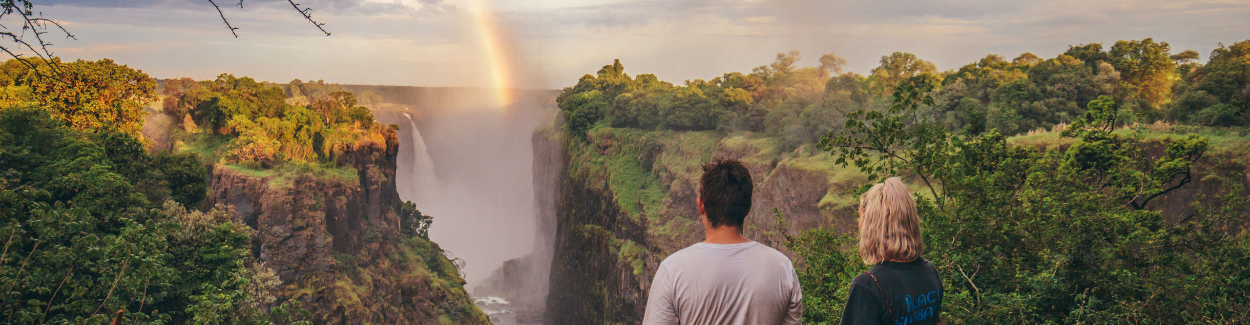 Couple looking at rainbow over Victoria Falls, on a cloudy day, Zimbabwe, Africa