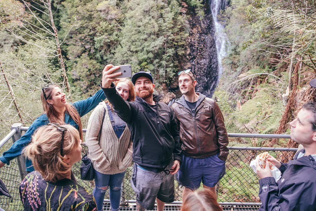 Travellers posing in front of a waterfall in the Tarkine Rainforest, Tasmania, Australia