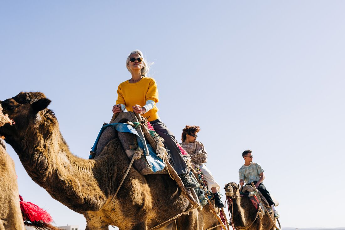 Intrepid travellers riding camels along the ocean shore at Essaouira