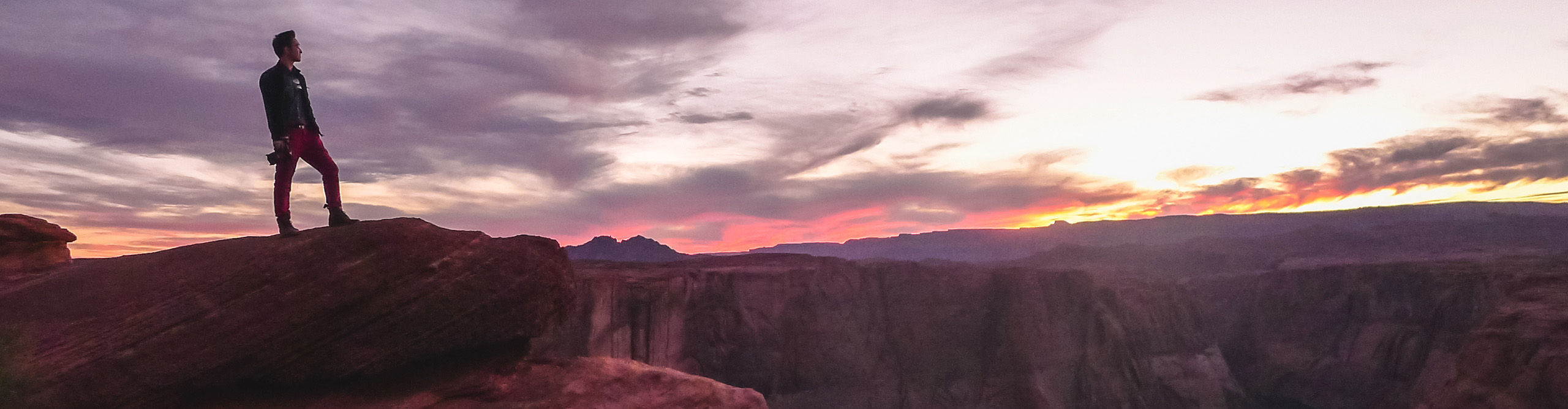 Photographer standing on top of Horseshoe Bend overlooking Colorado River at sunset, Arizona, USA