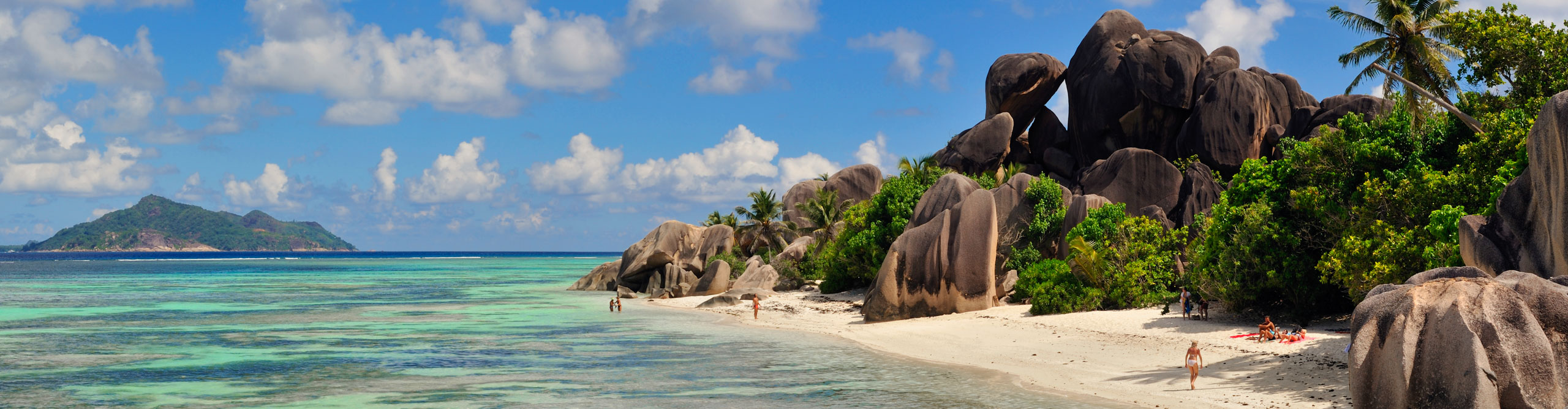 People on Source d'Argent beach, with a bright blue sky and turquoise water in the Seychelles
