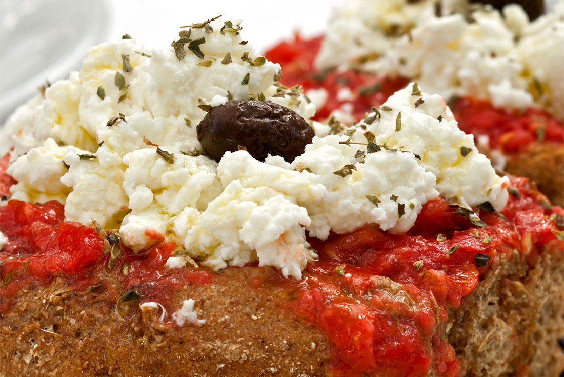 Closeup shot of Dakos salad, a Cretan dish of rye bread husks with feta, fresh tomatoes, olives, onion, and oregano