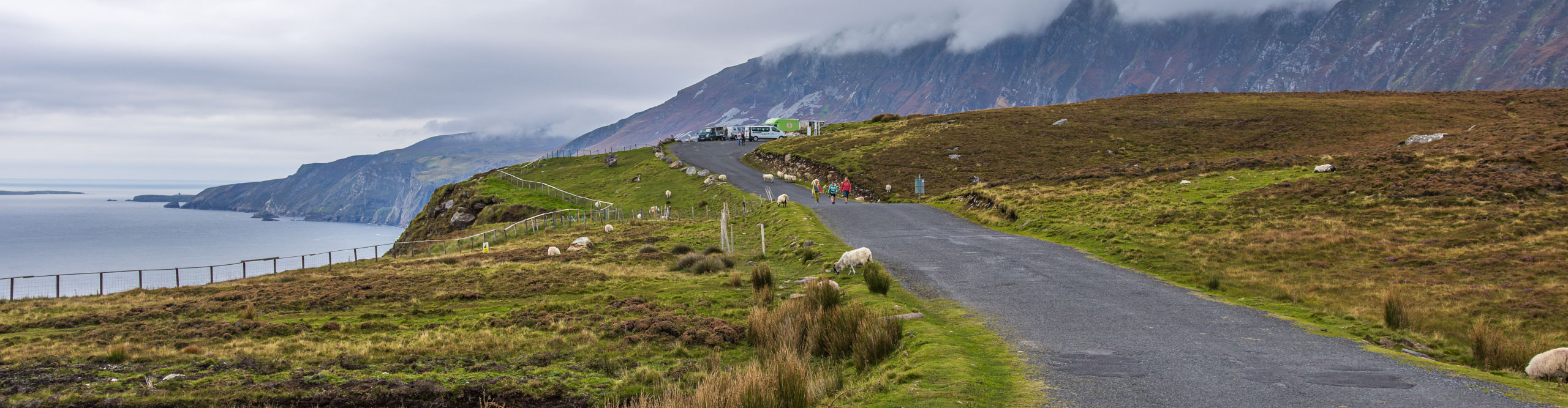 People and sheep on road near the water in Teelin, Ireland on a cloudy day 