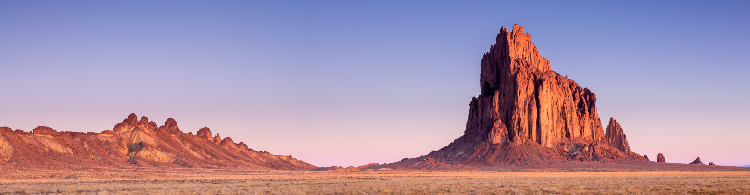 Shiprock, at sunset with a pink and purple skin and the rock illuminated in red, New Mexico, USA