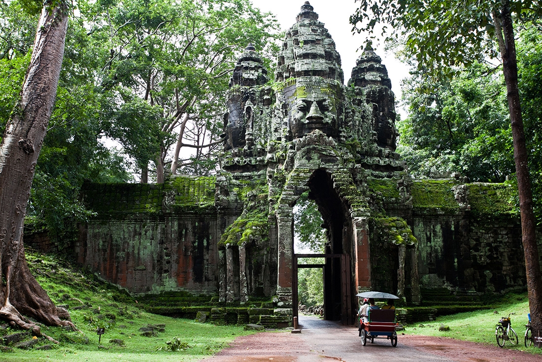 Travellers arriving by tuk-tuk to the entrance of a temple in the Angkor region in Cambodia.