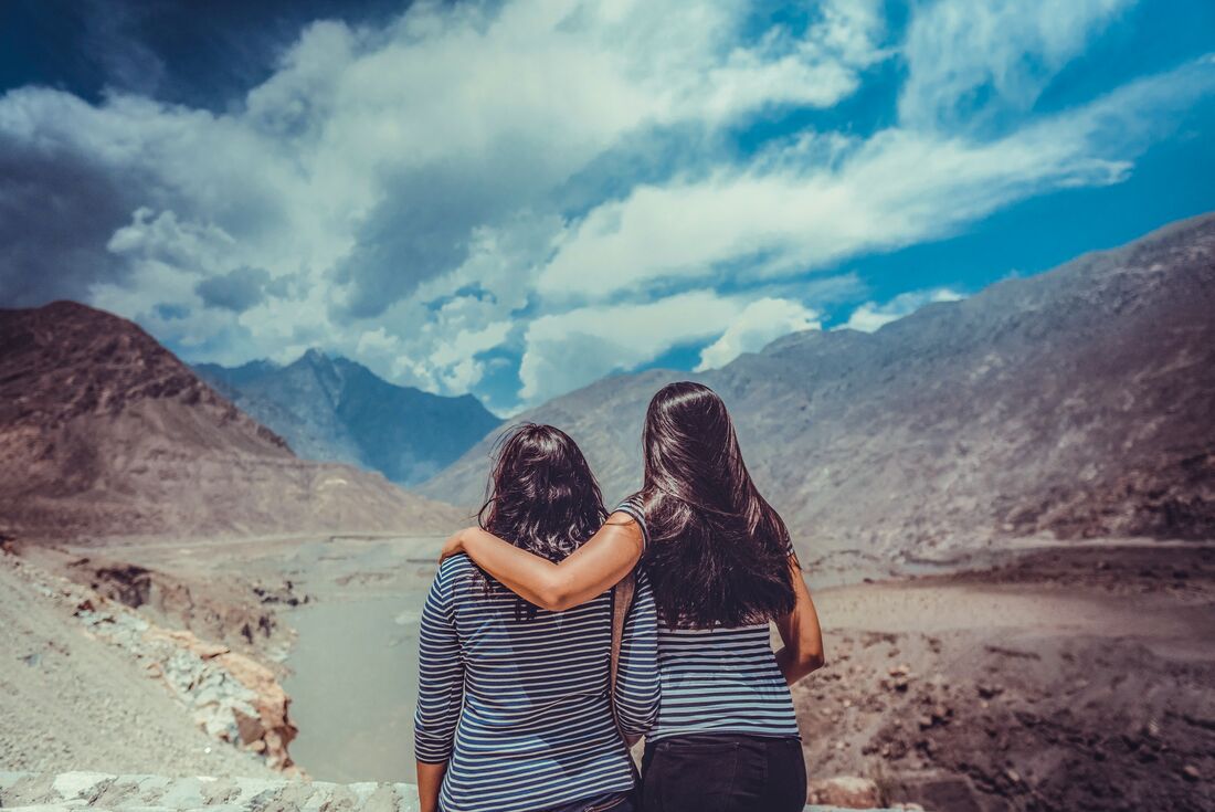 Two female travellers embrace and look out at the hunza mountain ranges 