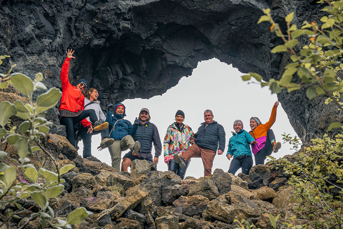 Group of travellers stand inside an arch of volcanic stone at Dimmuborgir Lava Field