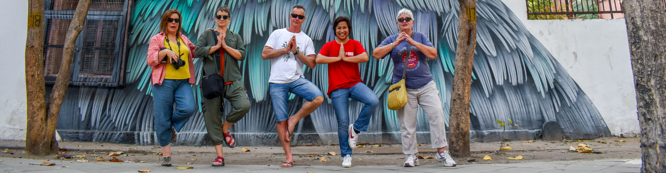 Group doing yoga pose and smiling in front on a mural in the Lodhi Art district in Delhi, India 