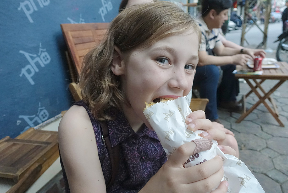 Girl eating banh mi, a local street food, outside the restaurant in Hoi An, Vietnam on an Intrepid Travel tour.