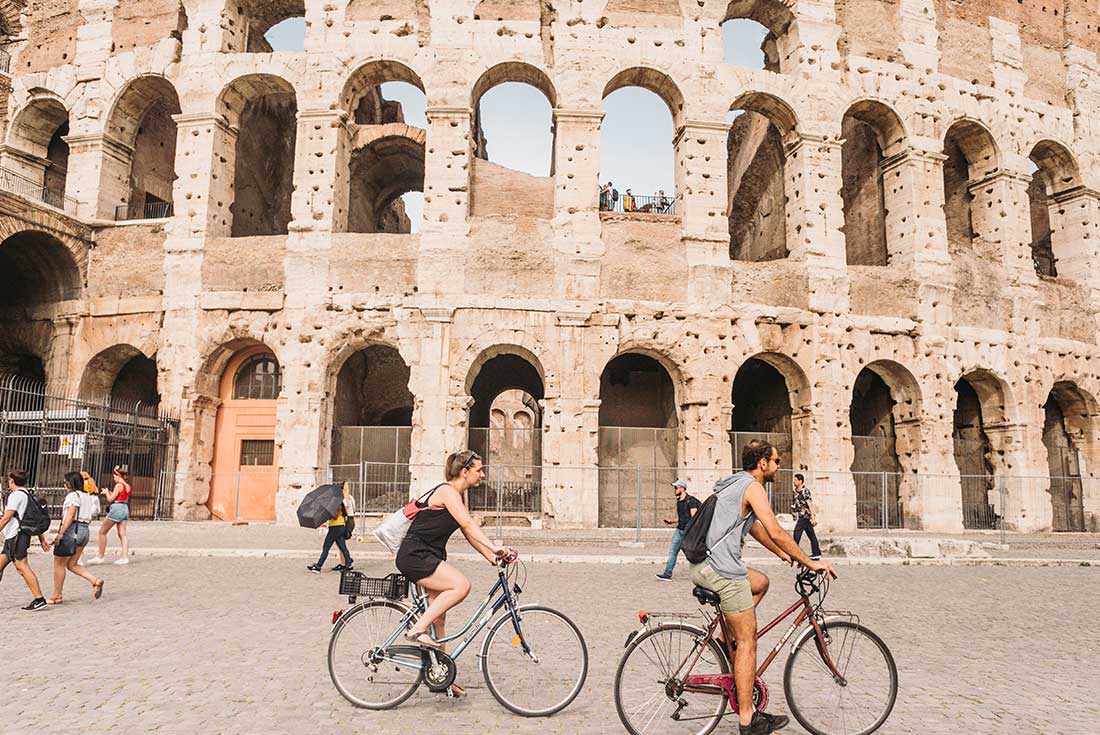 Two travellers cycle past the Colosseum in Rome