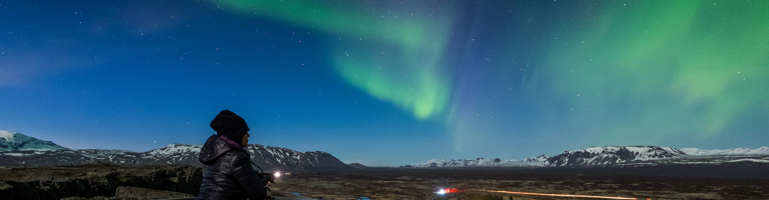 Traveller looks out at Northern Lights in Thingvellier National Park in Iceland