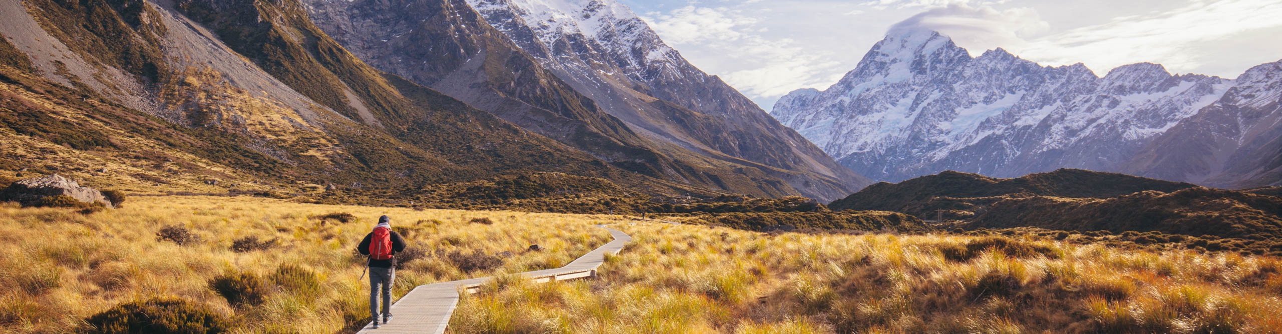 Hiker walking along the path towards Mount Cook, with the sun behind the mountains, New Zealand 