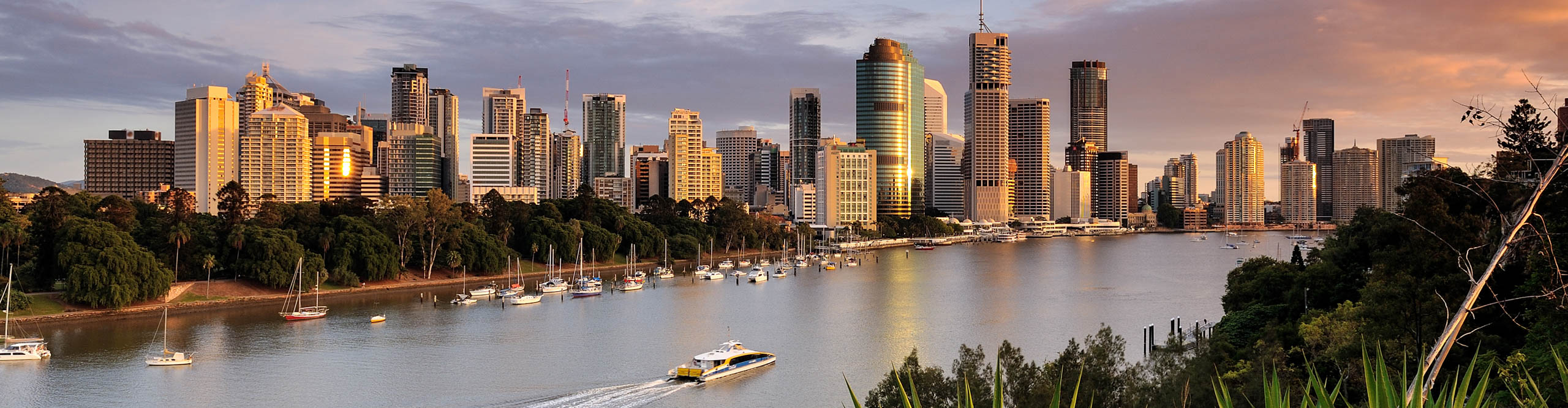 Brisbane river at sunset with boats sailing through and the buildings glowing orange