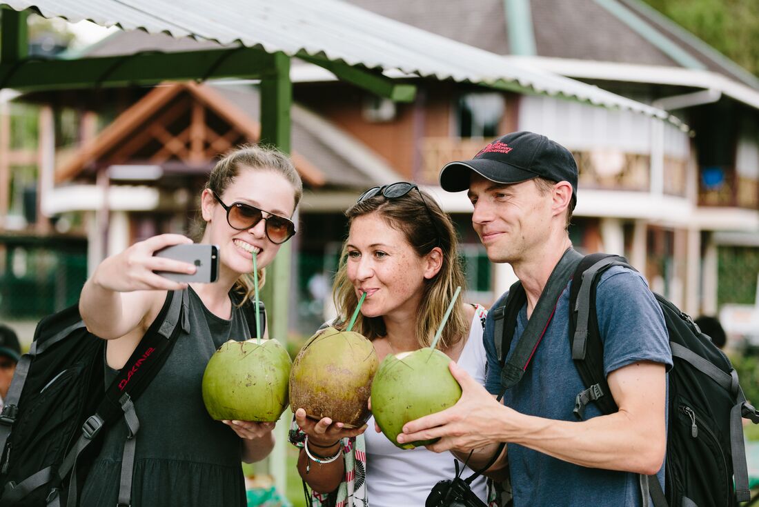 Three travellers taking a picture of themselves drinking out of a coconut in Borneo