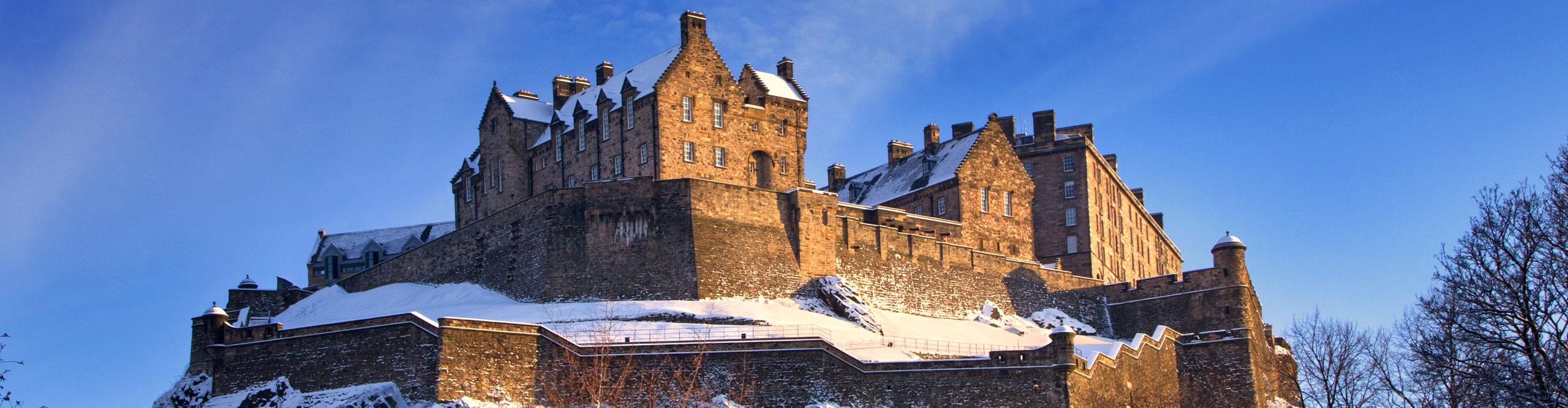 Edinburgh castle dusted with snow glows in the late afternoon winter sunset, with bright blue skies