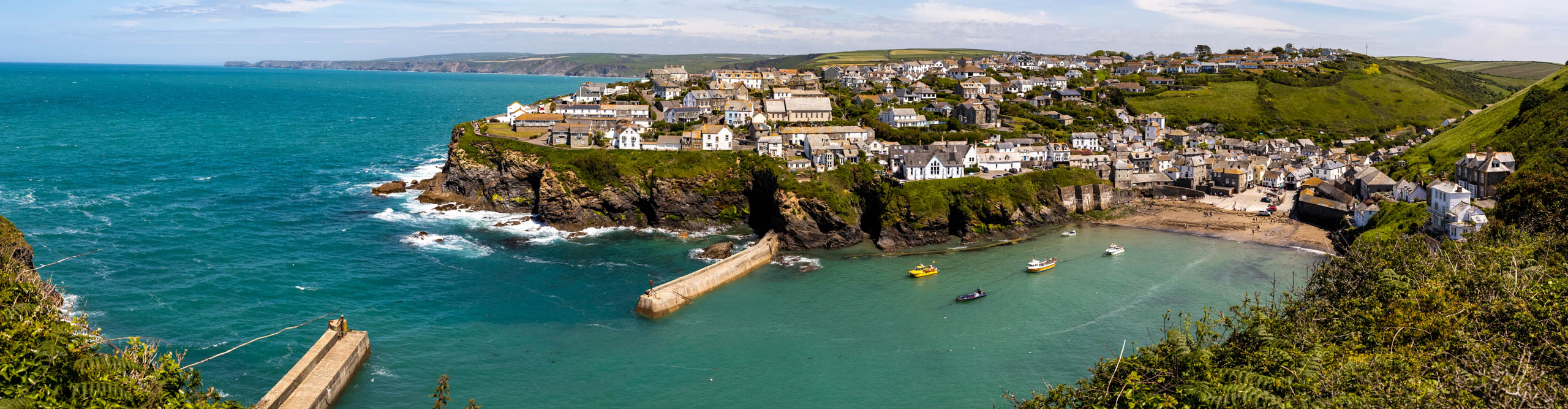 View of coastal town of Port Isaac with boats in the water, in spring with a bright blue sky 