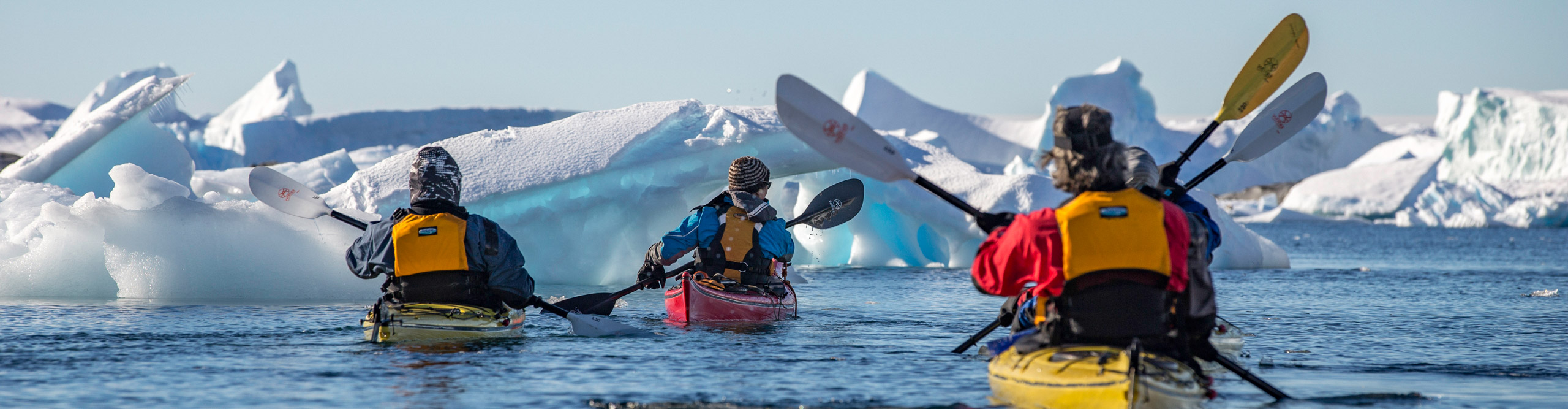 Group kayaking across the water near icebergs on a clear sunny day in Antarctica 