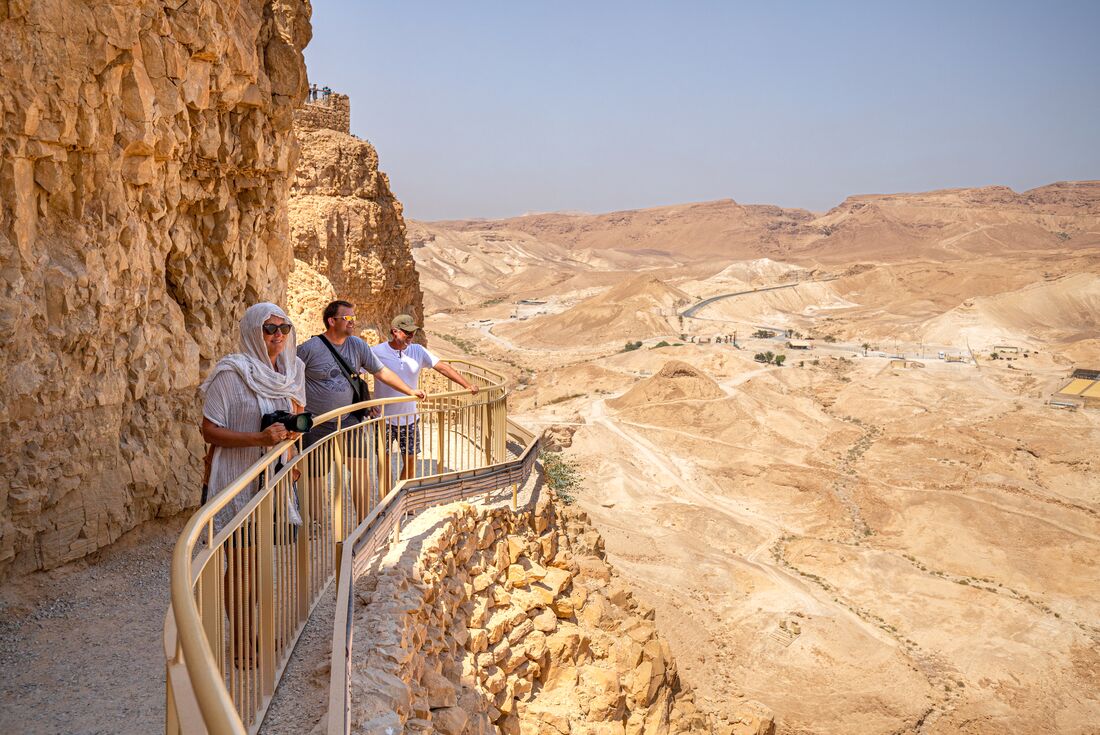 Travellers look out over the rocky landscape of Masada on a sunny day
