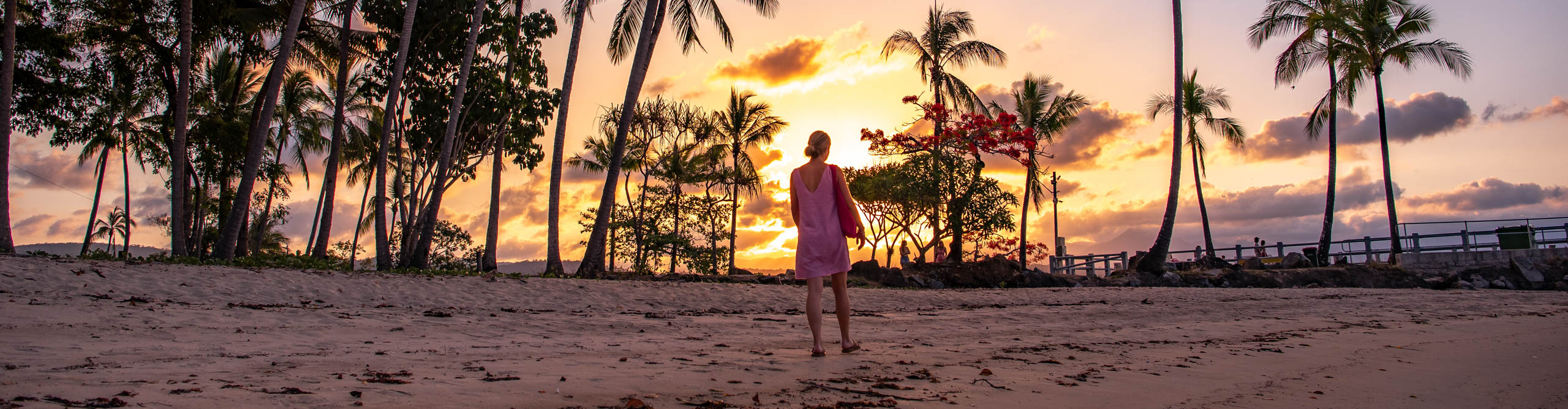 Woman walking along the beach with palm trees in Port Douglas at sunset 