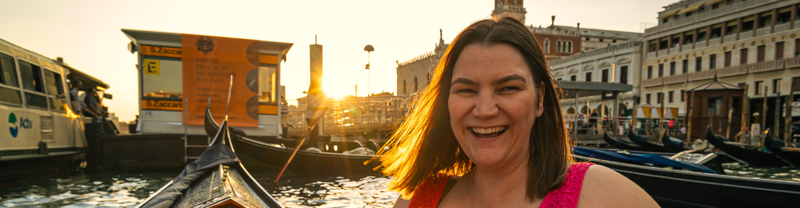 Woman in a red dress laughing on a gondola at sunset on the canals of Venice, Italy 