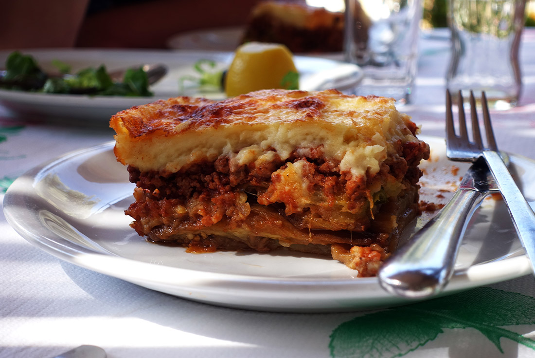 A plate of a traditional Greek dish called Moussaka on a rustic outdoor table