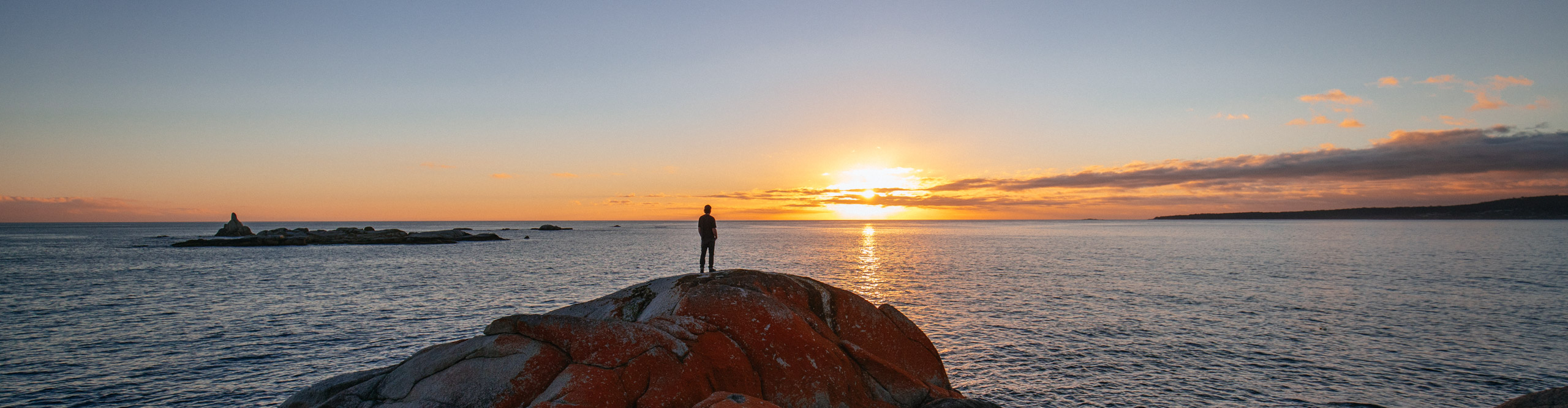 Traveller looking at the sunset from the rock of the Bay Of Fires, Tasmania, Australia 