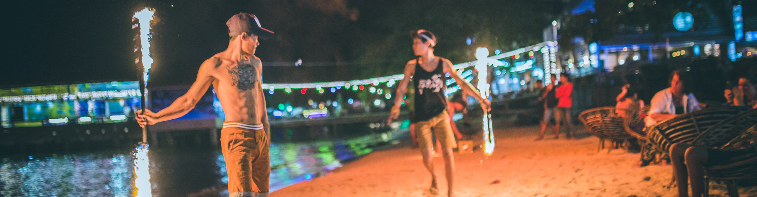 People fire dancing on the beach with water in the distance and coloured light at night, Cambodia