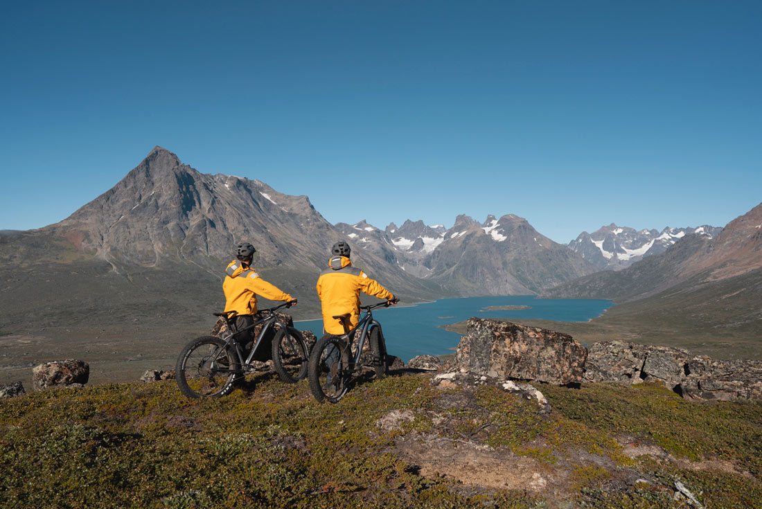 Travellers mountain biking across West Greenland with mountains in the background