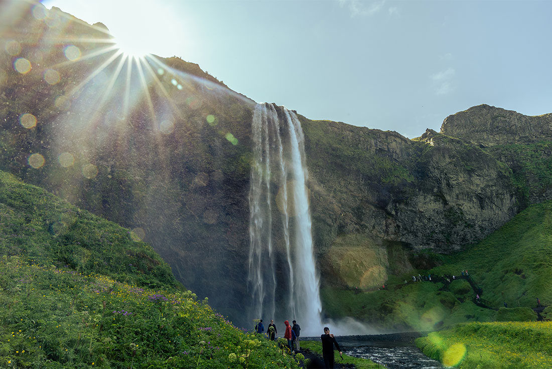 Group of travellers walk into the Seljalandsfoss Waterfall